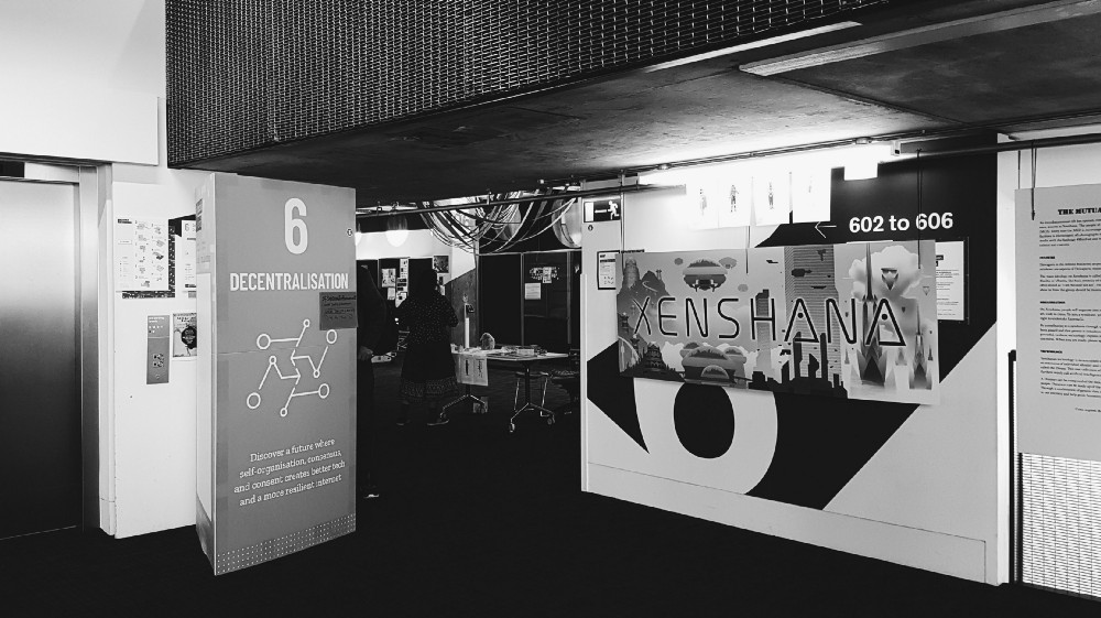 Photograph of the entrance of the Decentralisation space, showing both their explanatory sign and a big Xenshana poster.