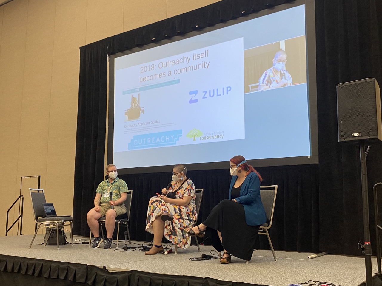 Sage, Karen, and I share the stage to talk about Outreachy. In this photo, I’m in the middle seat, holding a microphone and talking about how community understood itself as a community.